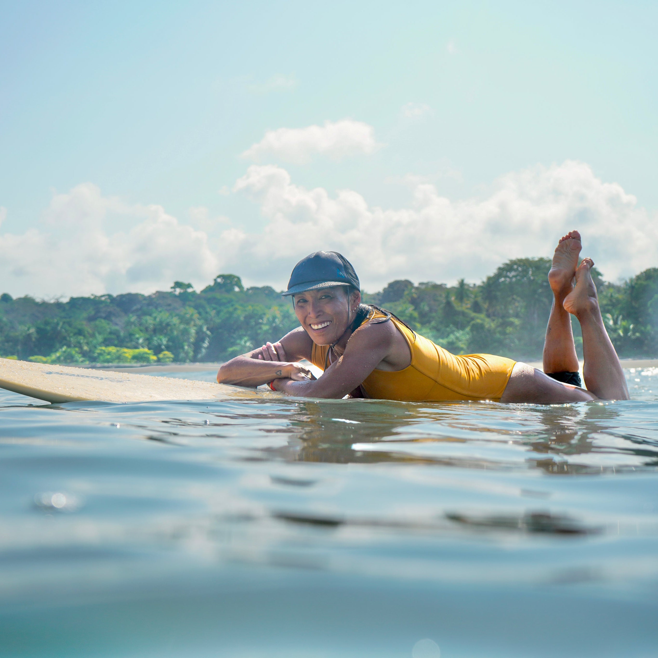 Person lying on a surfboard in the water with a scenic background